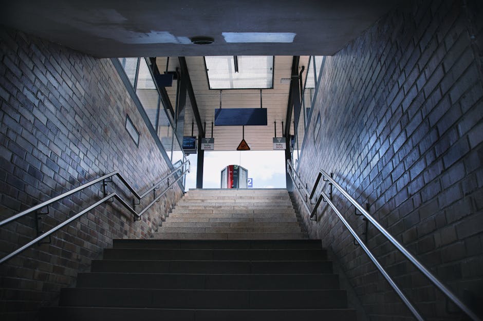 A view of a London train station platform during sunrise, with train tracks curving towards a tunnel illuminated by the ambient light. The platform features tactile paving in yellow and black strips a